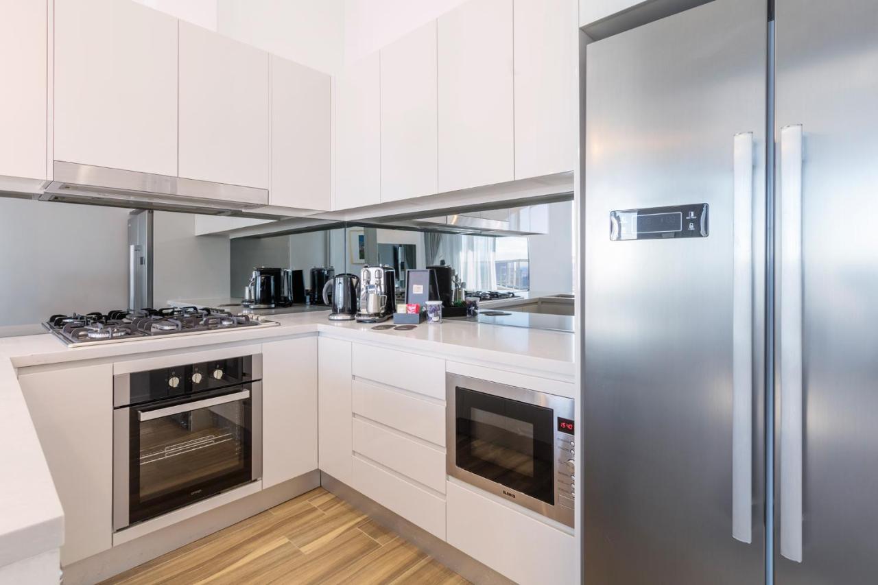 邦迪交界处美利通公寓式酒店 悉尼 外观 照片 The photo shows a modern kitchen with a clean and minimalist design. It features white cabinetry and a stainless steel refrigerator. The kitchen includes a gas stove with an oven below it, as well as a microwave. There are several kitchen appliances,