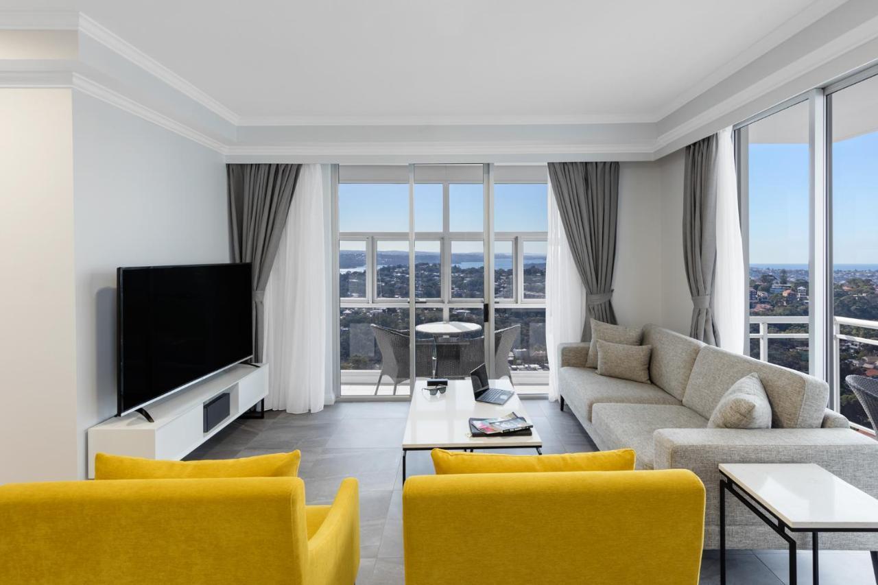 邦迪交界处美利通公寓式酒店 悉尼 外观 照片 The photo depicts a modern living room space with large windows that offer a view of the outside. The decor is minimalist and stylish, featuring a light color palette. 

In the center, there are two bright yellow chairs facing each other. A sleek, re