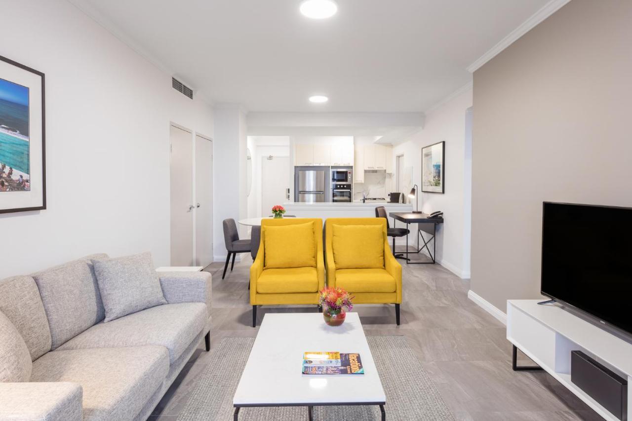 邦迪交界处美利通公寓式酒店 悉尼 外观 照片 The photo shows a modern living space with a light and airy design. In the foreground, there are two bright yellow armchairs flanking a white coffee table, which has a small vase of flowers and a magazine on it. To the left, there is a light gray sof