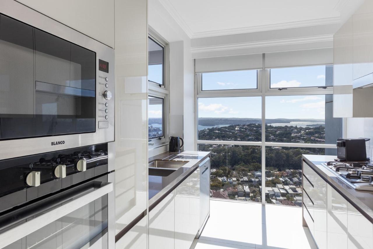 邦迪交界处美利通公寓式酒店 悉尼 外观 照片 The photo shows a modern kitchen with sleek, shiny white cabinets and a large window that offers a panoramic view of the outside landscape. The kitchen features built-in appliances, including an oven and a stove, with a stylish countertop. The spacio
