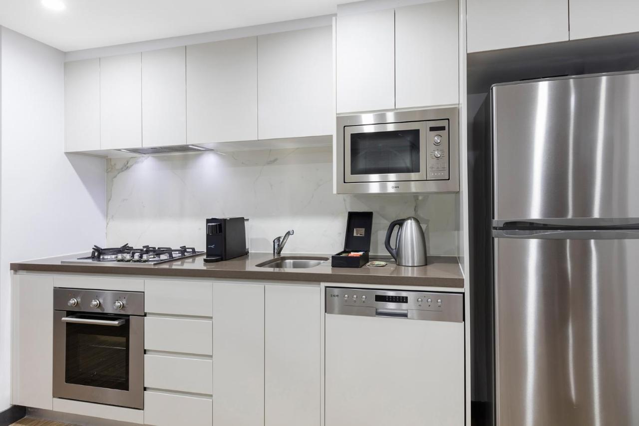 邦迪交界处美利通公寓式酒店 悉尼 外观 照片 The photo shows a modern kitchen with a sleek, minimalist design. It features white cabinetry and a countertop that blends with the overall aesthetic. 

Key elements include:

- A stainless steel refrigerator on the right.
- An oven with a gas cookto