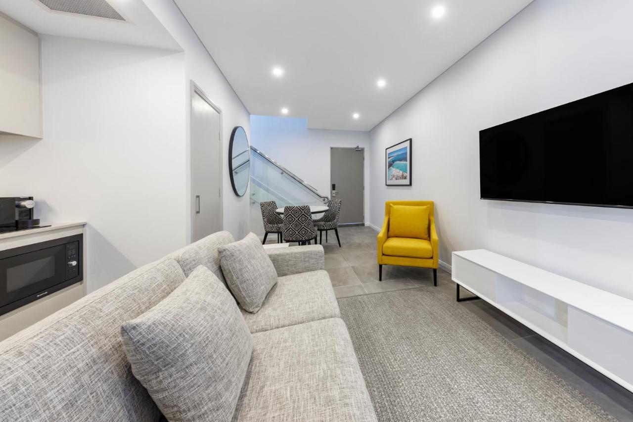 邦迪交界处美利通公寓式酒店 悉尼 外观 照片 The photo shows a modern and stylish living space. It features a light-colored sofa with cushions, positioned to face a wall-mounted flat-screen TV. There's a yellow accent chair nearby that adds a pop of color to the room. The décor is minimalistic,
