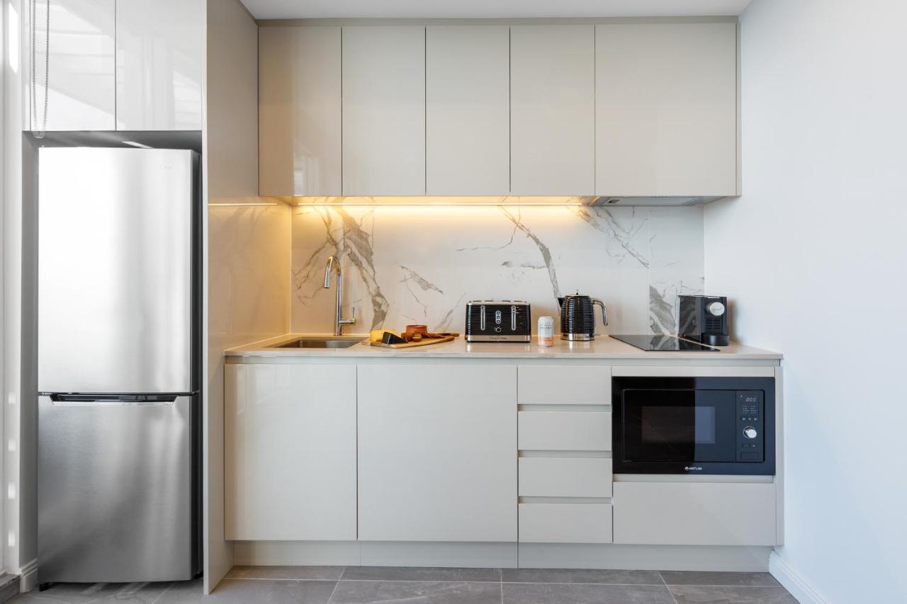 邦迪交界处美利通公寓式酒店 悉尼 外观 照片 The photo shows a modern kitchen featuring a sleek design. It includes light-colored cabinetry with a smooth finish and upper cabinets that blend seamlessly with the wall. The countertop is made of a light stone, complementing the overall aesthetic. 