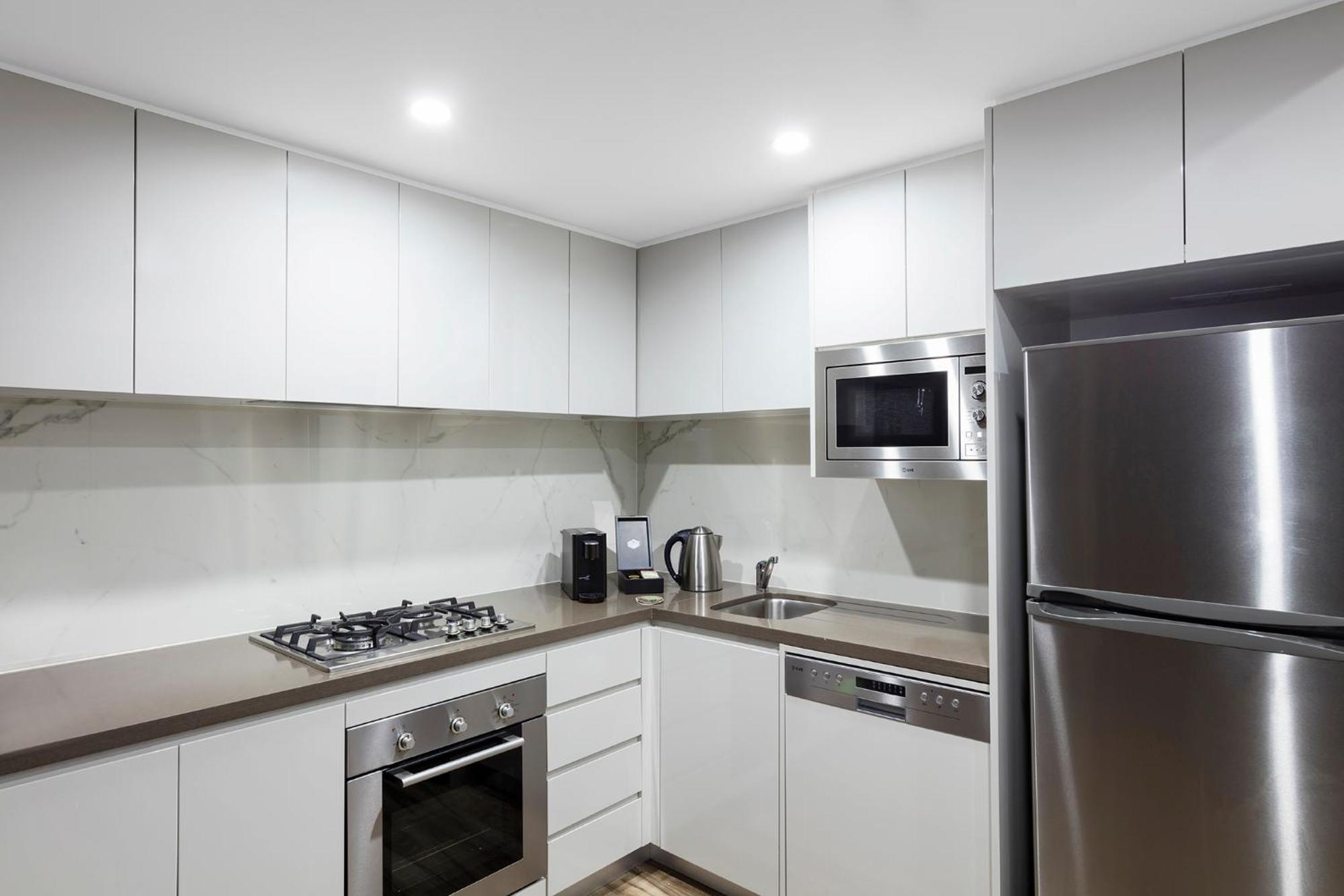 邦迪交界处美利通公寓式酒店 悉尼 外观 照片 The photo shows a modern kitchen featuring a minimalist design. It has light-colored cabinetry, a countertop, and stainless steel appliances. The appliances include a gas stove with multiple burners, an oven, a microwave, a kettle, and a refrigerator